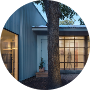 - Oasis Builders, Inc. Blue exterior building with large front windows, and a tree in the foreground; doorway visible on the left.