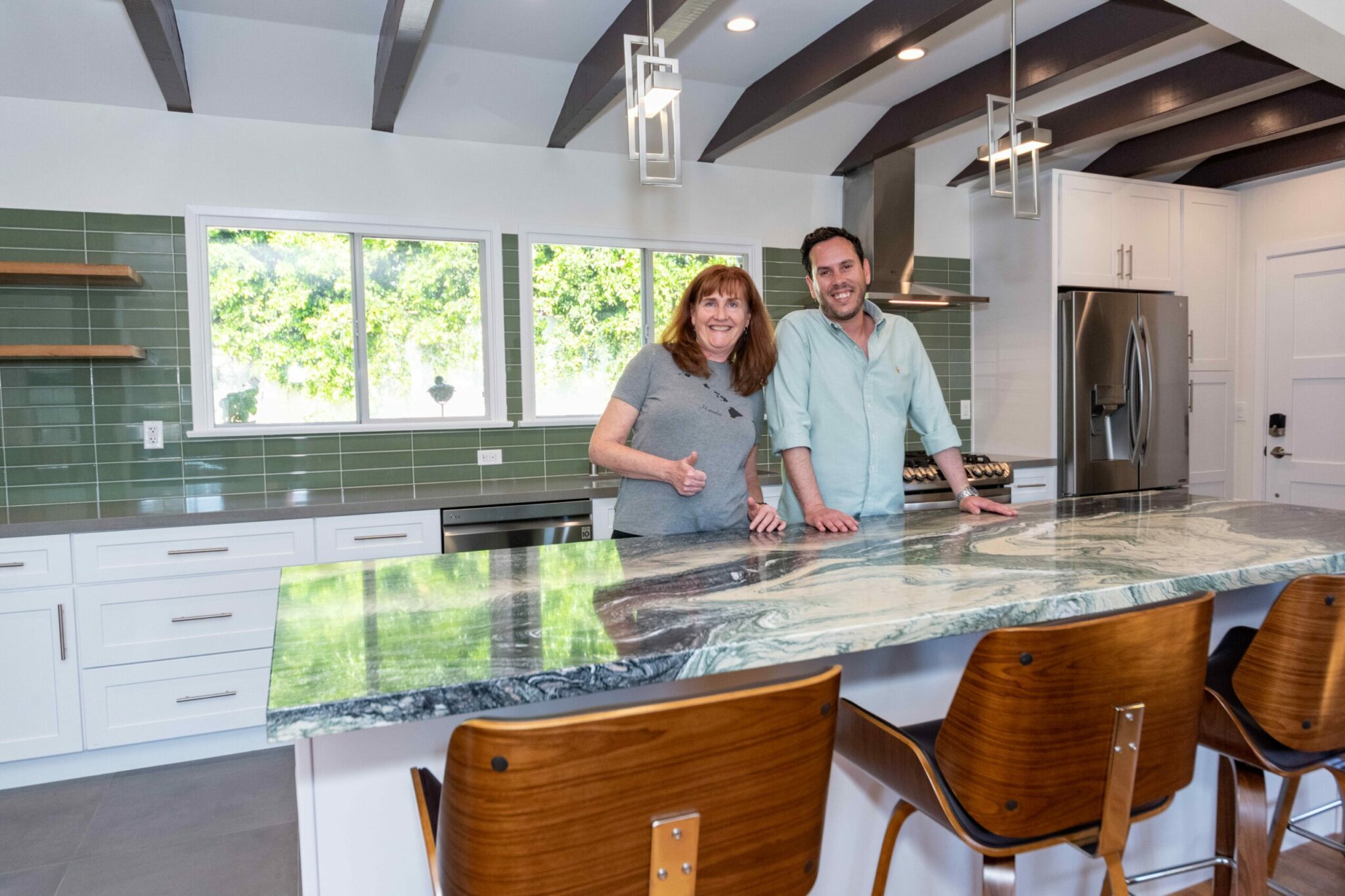oasis-builders-client-project-meeting - Oasis Builders, Inc. Two people stand at a marble kitchen island in a modern, bright kitchen with green tile backsplash and stainless appliances.