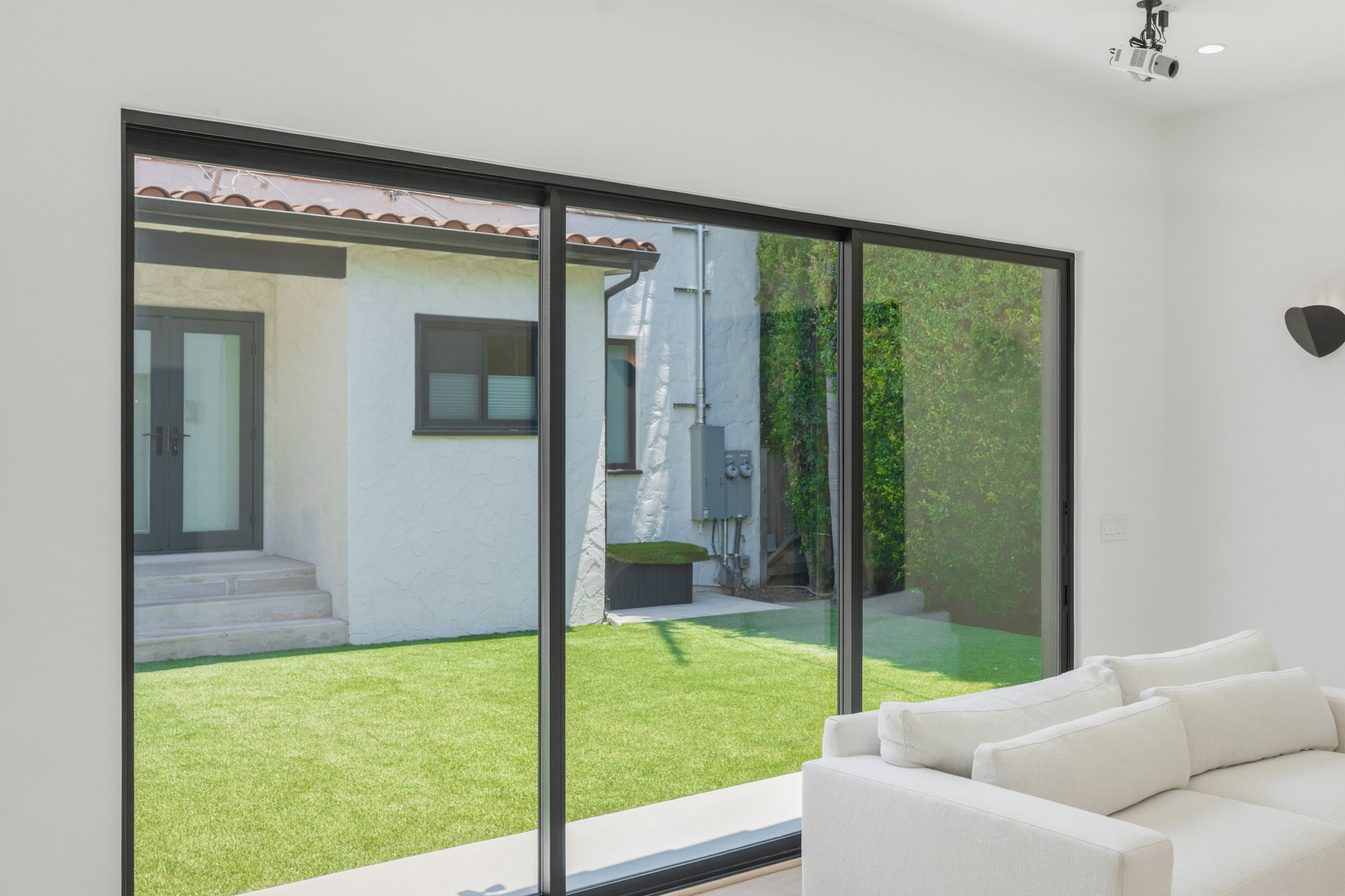 adu-living-room-with-large-sliding-glass-doors - Oasis Builders, Inc. Living room with large floor-to-ceiling sliding glass doors opening to a green backyard, a white sofa in the foreground.