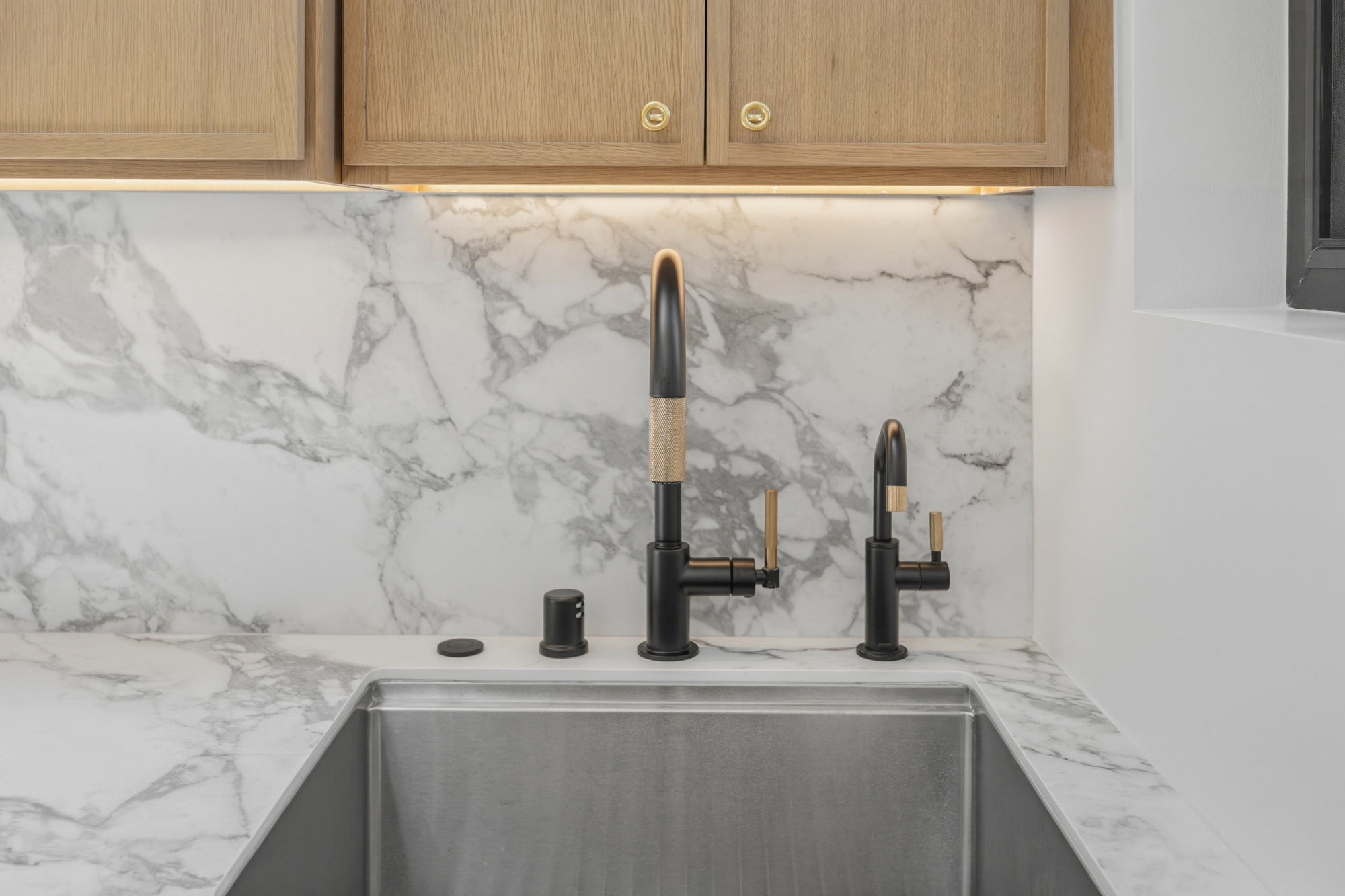 designer-kitchen-faucet-and-undermount-sink-detail - Oasis Builders, Inc. Modern kitchen sink area with a matte black faucet featuring brass accents and a marble backsplash.