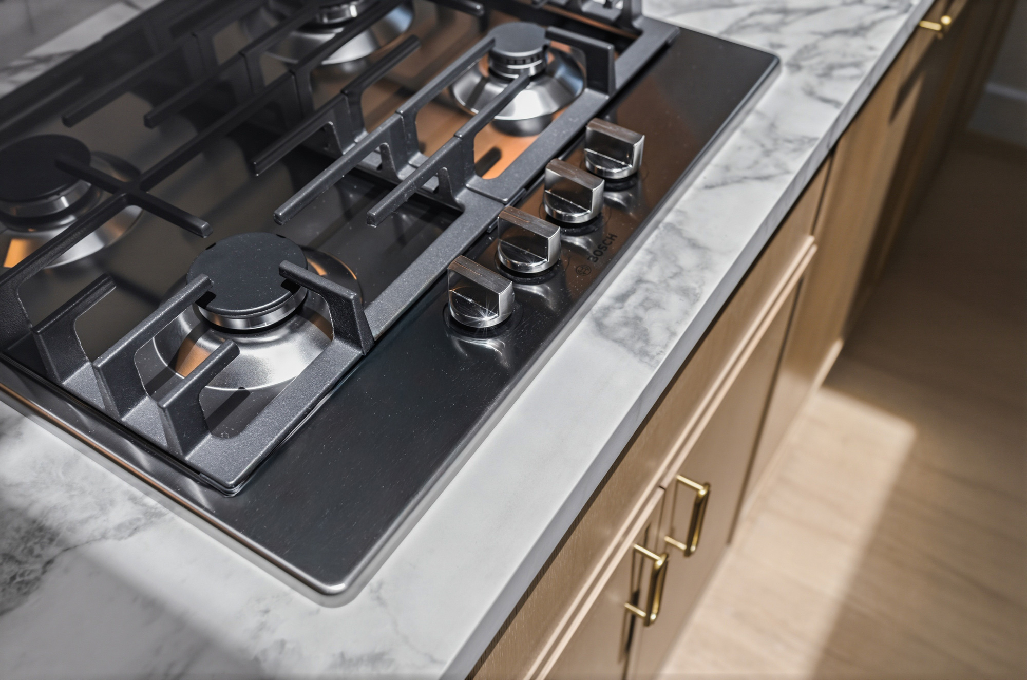 modern-adu-kitchen-bosch-gas-cooktop-detail - Oasis Builders, Inc. Close-up of a stainless steel gas cooktop with black grates and control knobs on a marble countertop.