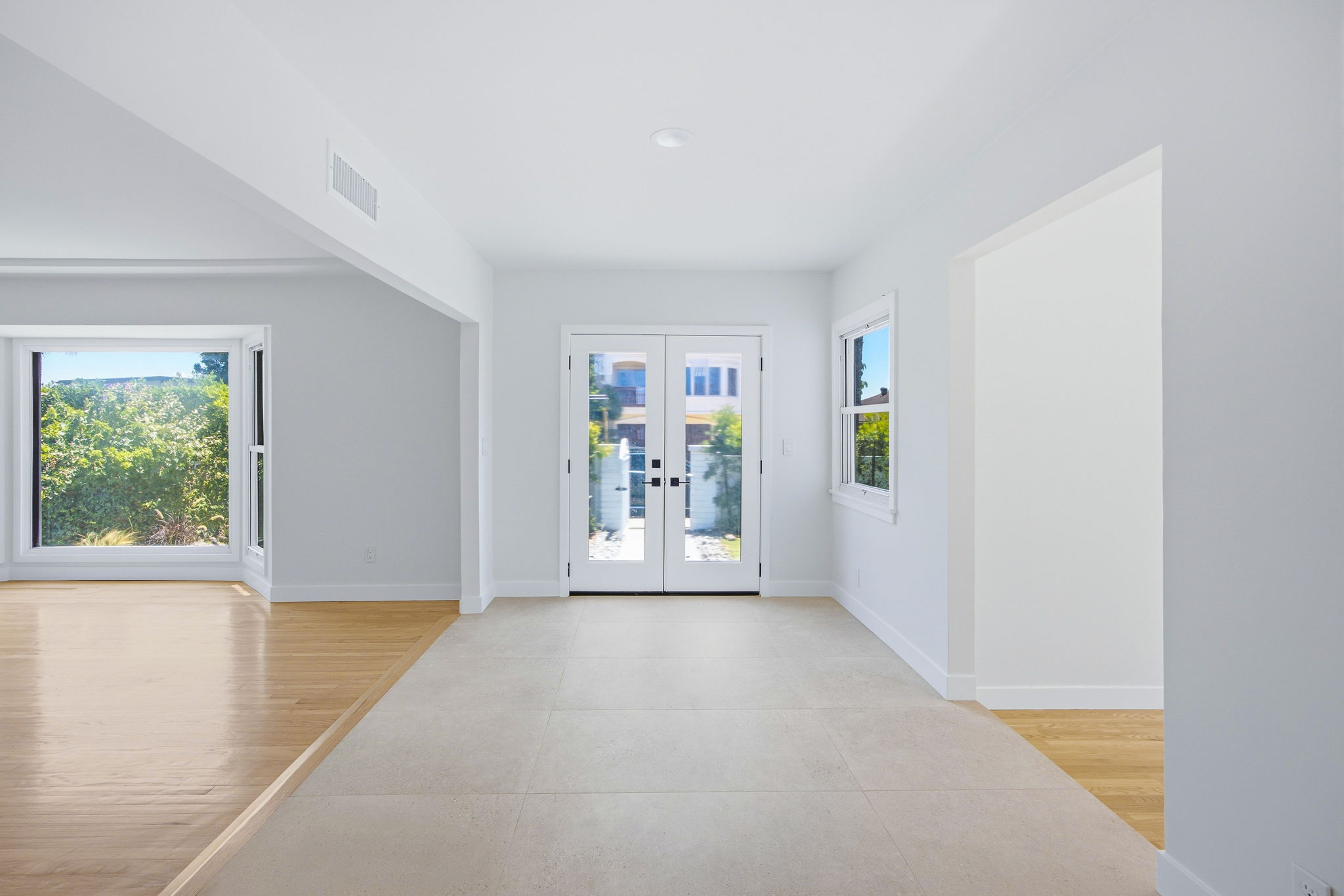 - Oasis Builders, Inc. Bright, empty entryway with double glass doors at the far end, gray walls, and mixed wood and tile flooring.