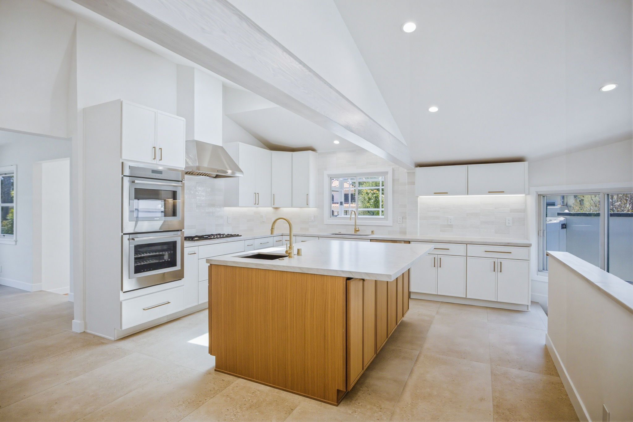 - Oasis Builders, Inc. Bright modern white kitchen with a large wooden island, stainless steel ovens, and white cabinets under soft recessed lighting