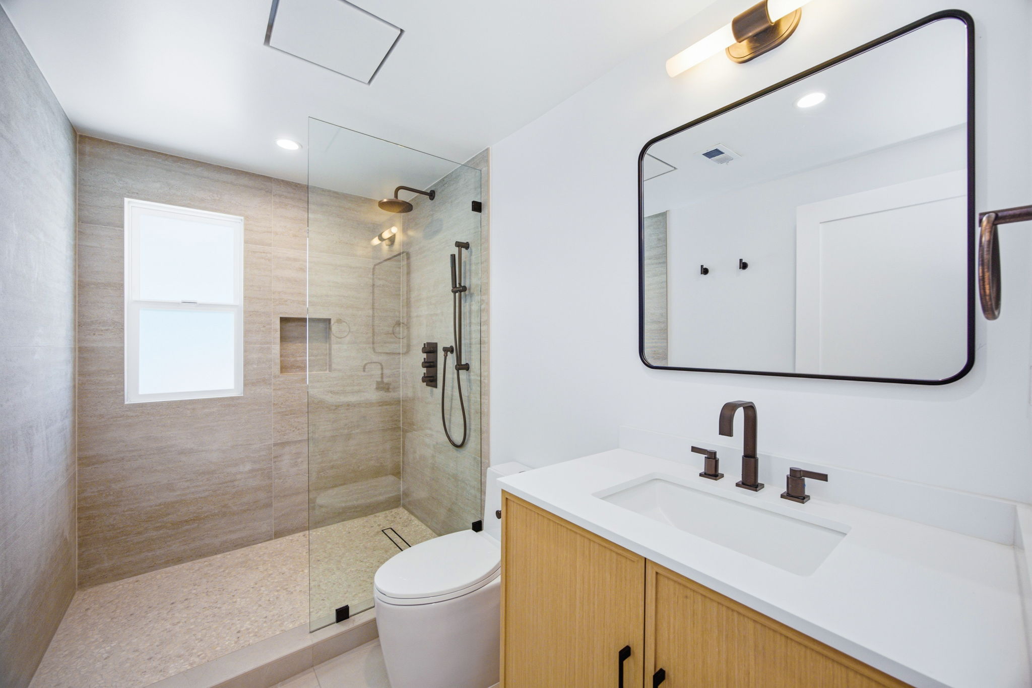 - Oasis Builders, Inc. Modern bathroom with glass-enclosed shower, beige tile, and black fixtures opposite a white countertop with a wooden vanity mirror