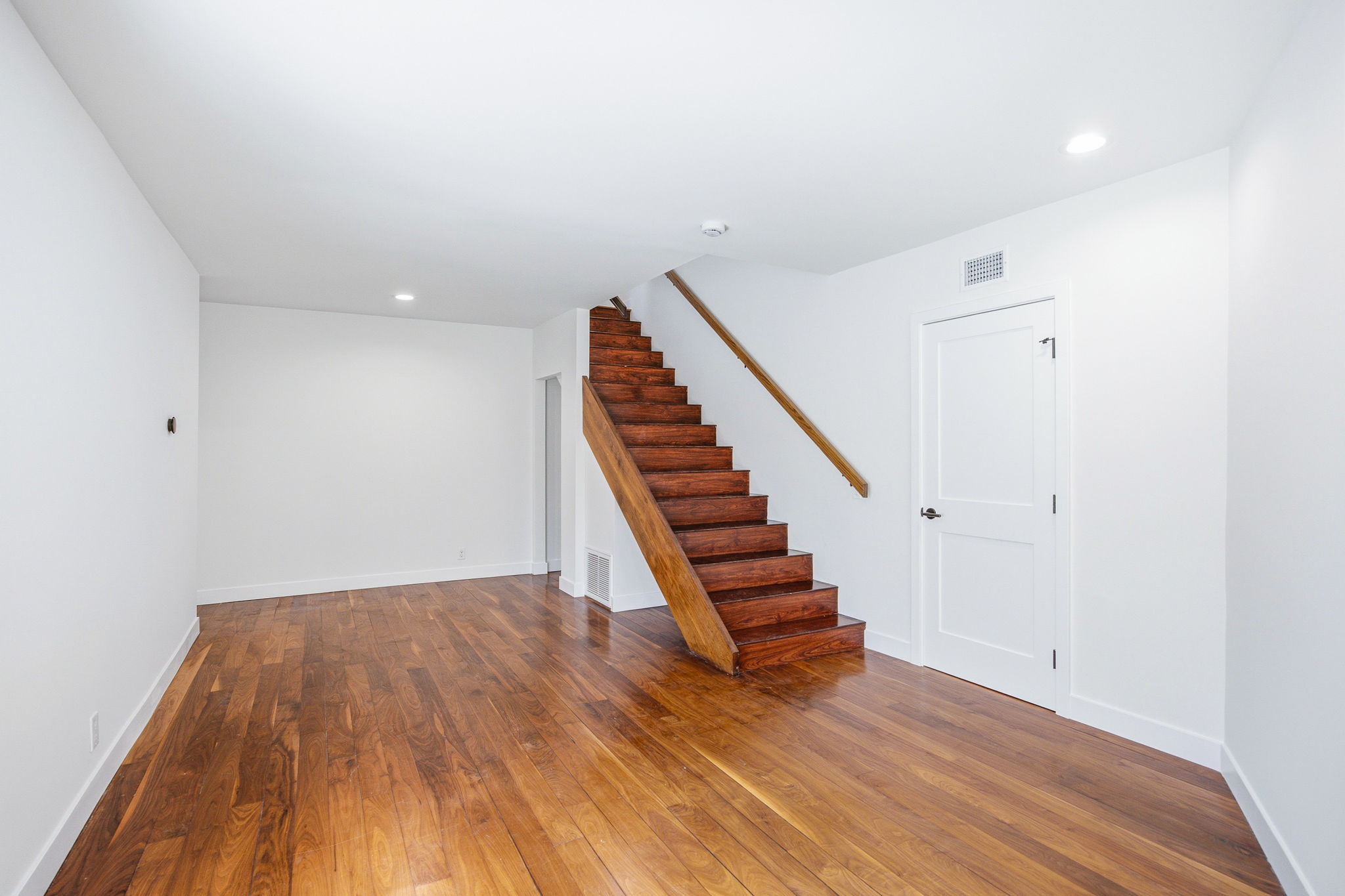 - Oasis Builders, Inc. Interior stairwell with wooden stairs and a white door at the base of the stairs; clean, bright hallway with hardwood flooring and white walls.